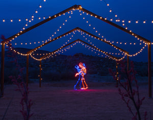 Two skeleton lovers dancing together created with light painting photography in the desert at night.