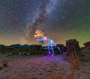 A T-rex dinosaur created with light painting photography in the Sierra Nevada beneath the Milky Way in a long-exposure night photo.